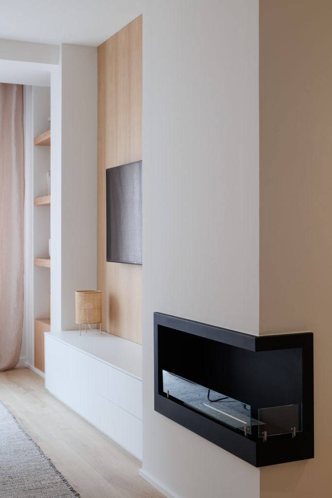 Chimenea de bioetanol empotrada en pared blanca con estantería de madera integrada y mueble a medida por Rocio Ramirez, experta en interiores